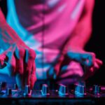 Hands of disc jockey playing electronic music set on stage in night club. Professional audio equipment on techno party
