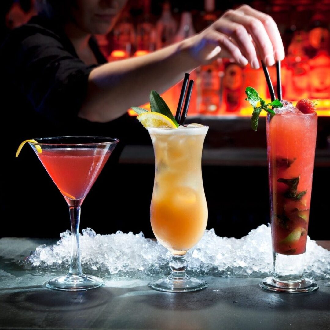 Three cocktails on ice at dimly lit bar
