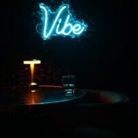 Blue neon 'Vibe' sign over dim bar table